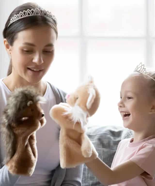 An au pair and young girl play with puppets.